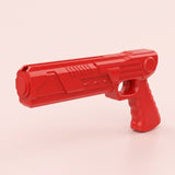 Red airplane launcher toy with a grooved grip and top launch channel stands alone against a pale pink background.