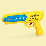 Yellow airplane launcher toy with a blue side panel, white arrow details, and red trigger stands against a pale yellow background.