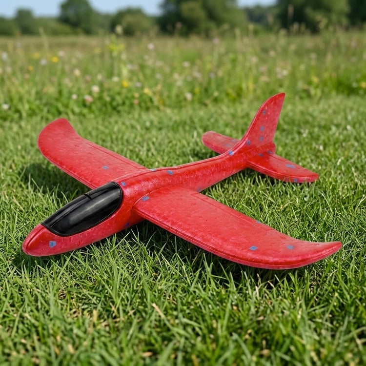 Red foam glider option for an airplane launcher toy, with blue flecks and a black cockpit, resting on green grass.