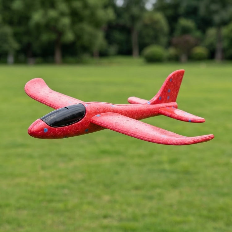 Red foam glider option for an airplane launcher toy, with blue flecks and a black cockpit, shown airborne over a green field.