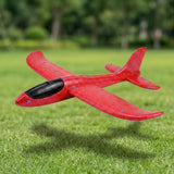 Red foam glider for an airplane launcher toy has blue speckles and a black cockpit, shown airborne above green grass.