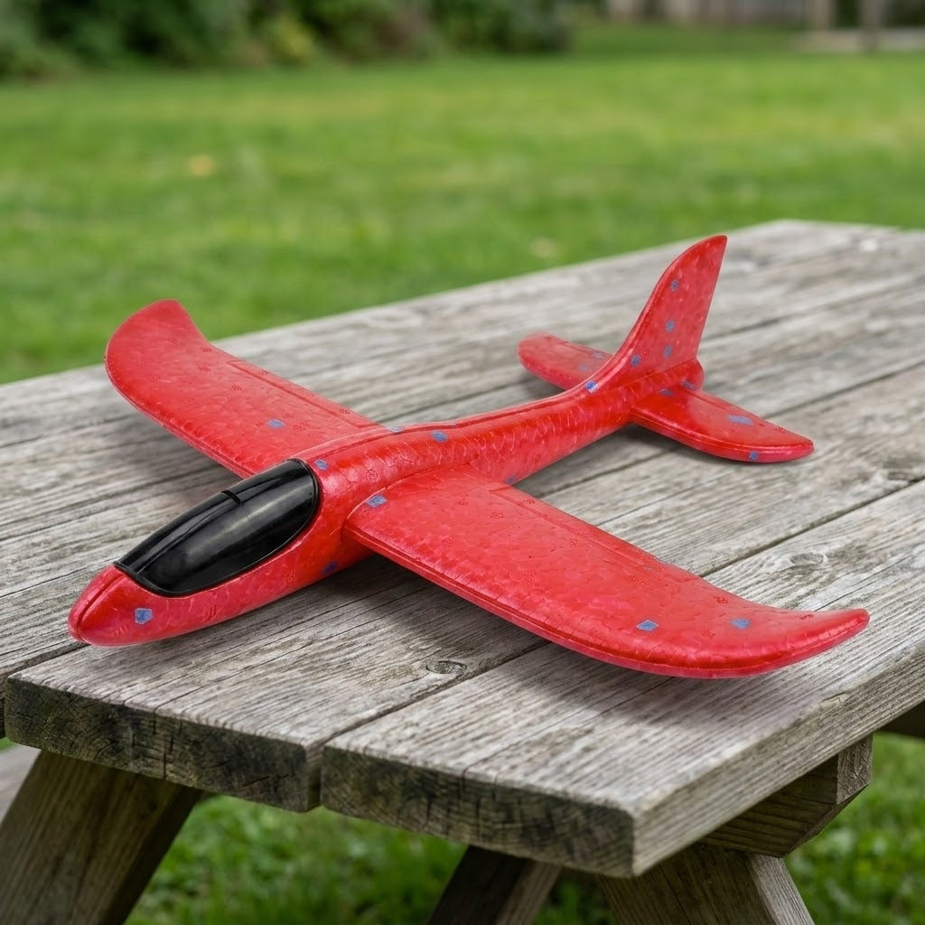Red foam glider for an airplane launcher toy has blue speckles and a black cockpit, resting on a weathered wooden picnic table.