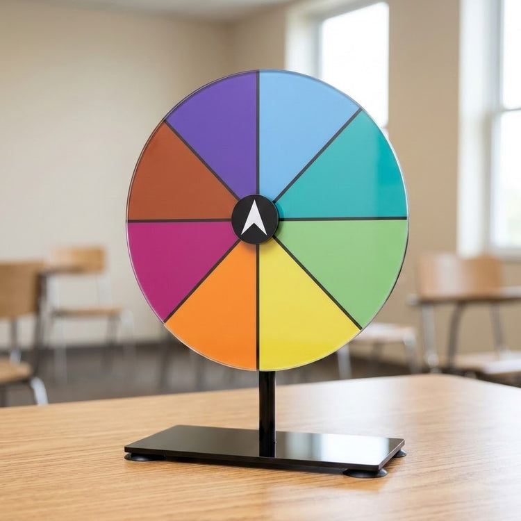 Multicoloured prize wheel with a white pointer and black suction-cup stand on a wooden classroom table.