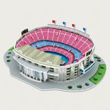 A 3D model or puzzle of a modern soccer stadium, featuring pink and blue seating, a gray roof, and green landscaping, shown on a light gray background.