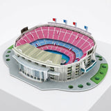 A plastic 3d stadium puzzle with pink and blue seating, pale gray walls and green landscaping sits on a white pedestal.
