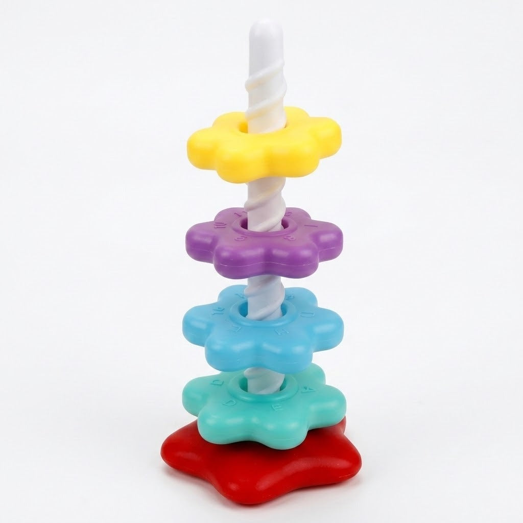 A plastic stacking toy has yellow, purple, blue and mint flower-shaped pieces along a white spiral post on a red base against white.
