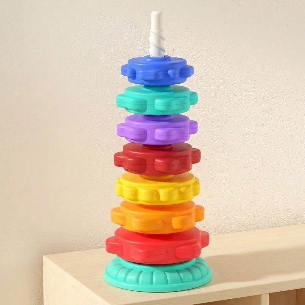 A stacking toy with seven colourful plastic rings, a white spiral post and mint base stands on a shelf against a cream wall.