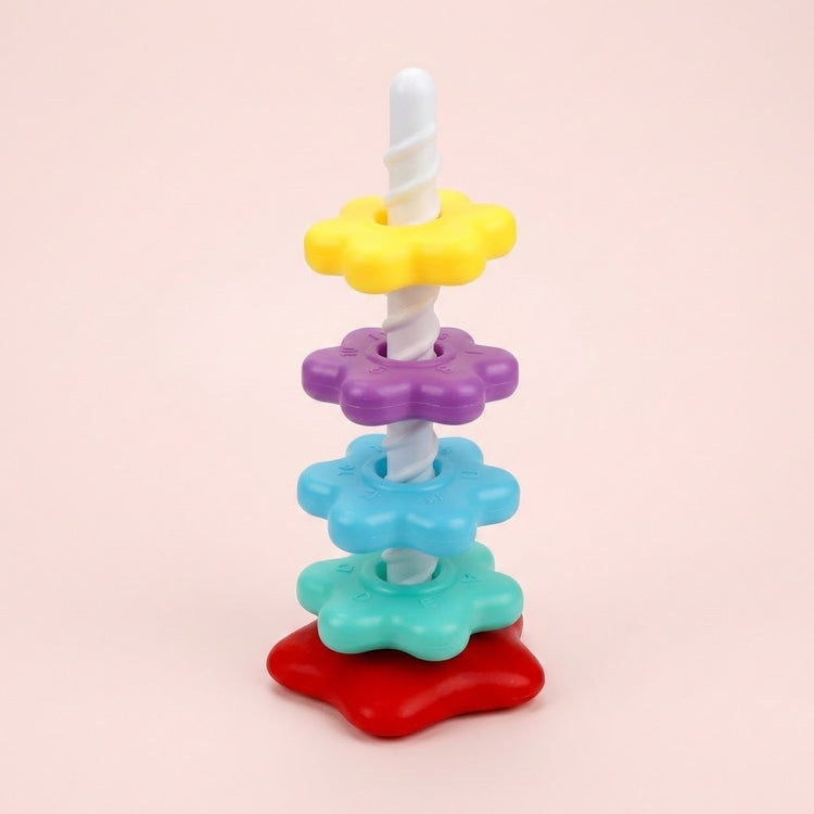 A stacking toy with yellow, purple, blue and turquoise flower-shaped rings, a white spiral post and red base stands against a pink background.