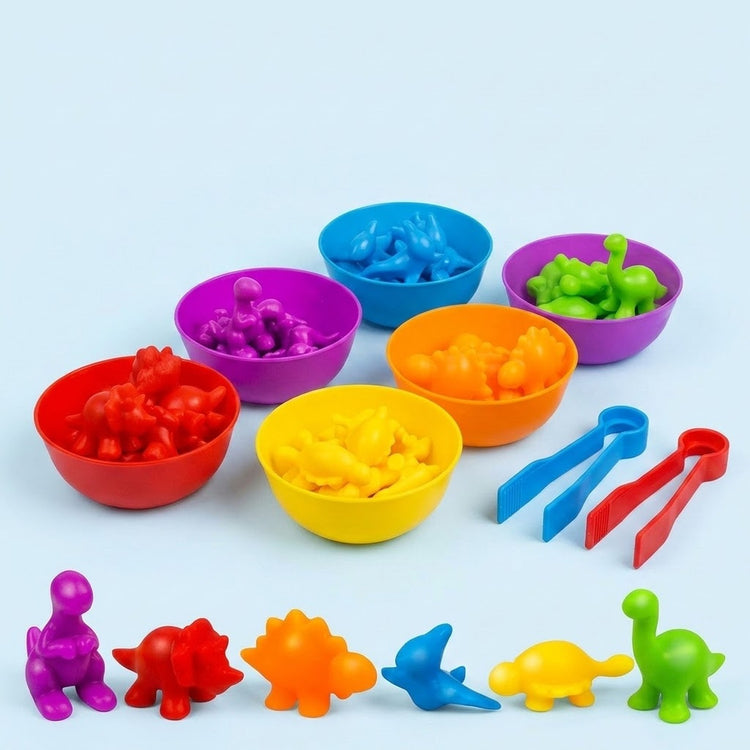 Sorting toy set with colourful dinosaur pieces in six plastic bowls, six loose dinosaurs and red and blue tweezers on a pale blue background.