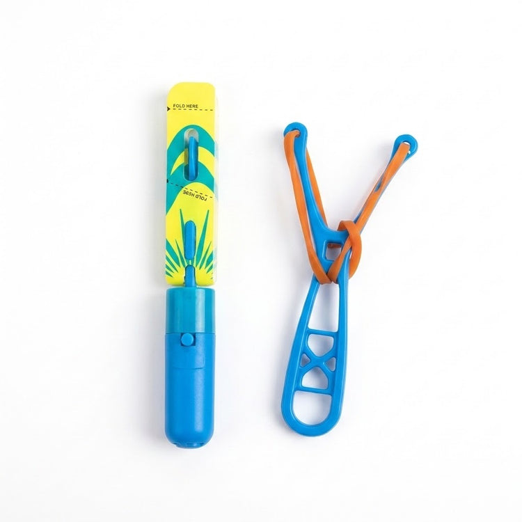 A blue slingshot helicopter with folded yellow and teal blades lies beside a blue launcher with orange elastic on white.