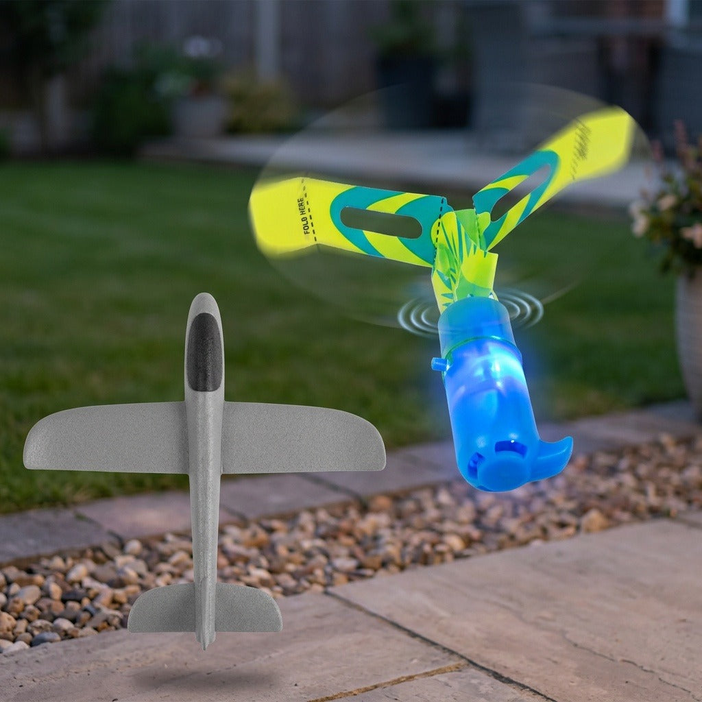 A blue slingshot helicopter with glowing blue light and yellow-green wings appears airborne beside a white toy airplane above a garden patio.