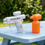 A white toy water gun labeled 'Prank Gun' spraying water toward an orange spray bottle on a light blue picnic table outdoors.