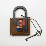Wooden lock puzzle with multicoloured mechanism pieces and a dark shackle lies beside its cord-attached key on a white background.