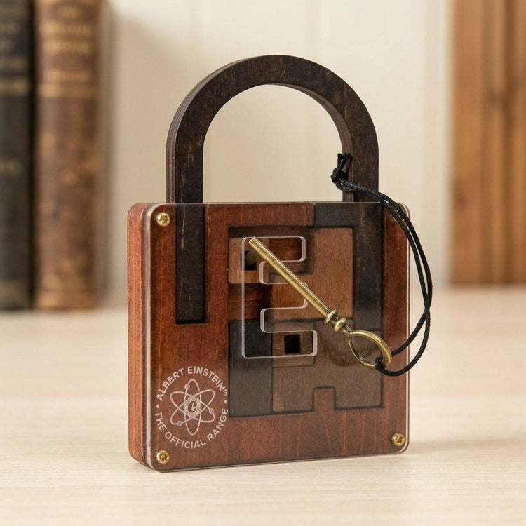 Brown wooden lock puzzle stands on a pale tabletop with its brass-coloured key across the clear front and blurred books behind.