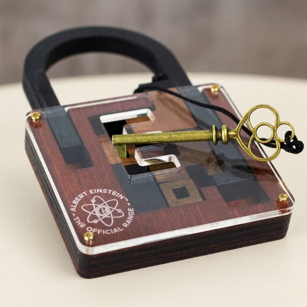 Reddish-brown wooden lock puzzle rests diagonally on a pale surface, with a brass-coloured key across its clear cover and layered edges visible.
