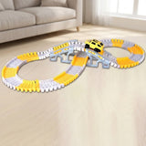 A children's toy train track set with yellow and white curved tracks, a gray bridge, and a small yellow train car, displayed on a light wood floor in a living room setting.