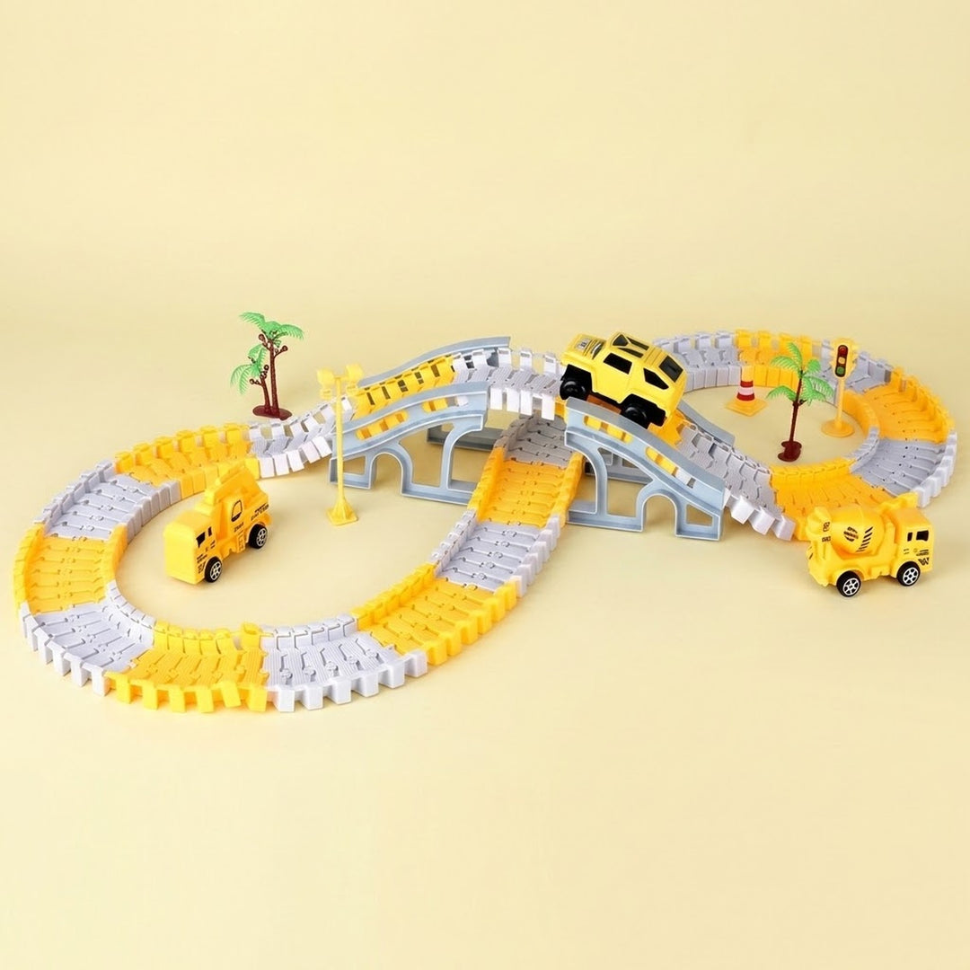 A children's toy construction-themed race track set with yellow and gray interlocking blocks forming an oval track, a small gray bridge, miniature palm trees, and three yellow toy vehicles including a car and two construction trucks, photographed on a plain beige background.