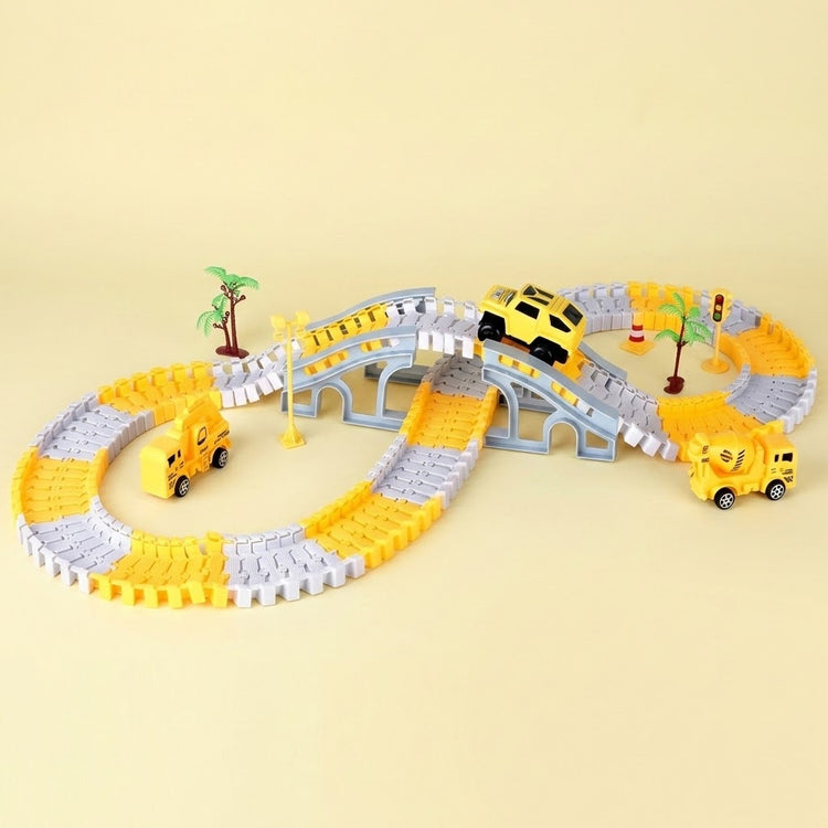 A children's toy construction-themed race track set with yellow and gray interlocking blocks forming an oval track, a small gray bridge, miniature palm trees, and three yellow toy vehicles including a car and two construction trucks, photographed on a plain beige background.