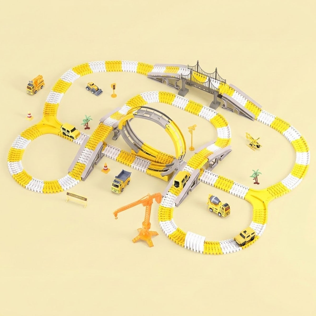 A children's toy train track set arranged on a pale beige background. The set includes a yellow and white looped track, a curved track section, a bridge, an orange crane, small toy cars, and tiny construction-themed accessories.