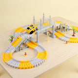 Yellow and gray car track set with a suspension bridge, yellow mini car, trees, and cones on a wooden table against pale yellow.