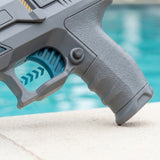 A close-up shows the gray electric water gun’s textured grip, blue trigger and round side button beside a turquoise pool.