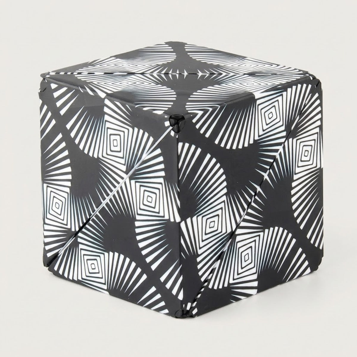 Black and white puzzle cube with radiating lines and nested diamond patterns shown folded closed against a light grey background.