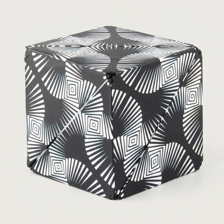 Black and white puzzle cube with radiating lines and nested diamond patterns shown folded closed against a light grey background.