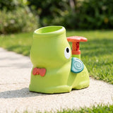 Lime-green elephant-shaped plastic disc launcher with a coral bow and teal ear sits on a sunlit garden path.