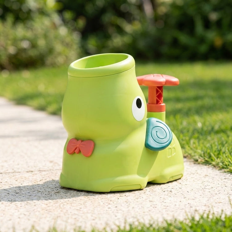 Lime-green elephant-shaped plastic disc launcher with a coral bow and teal ear sits on a sunlit garden path.