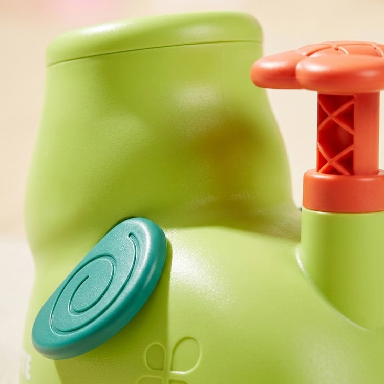 Close-up of the green plastic elephant disc launcher shows its teal spiral ear and raised orange pedal against a cream background.