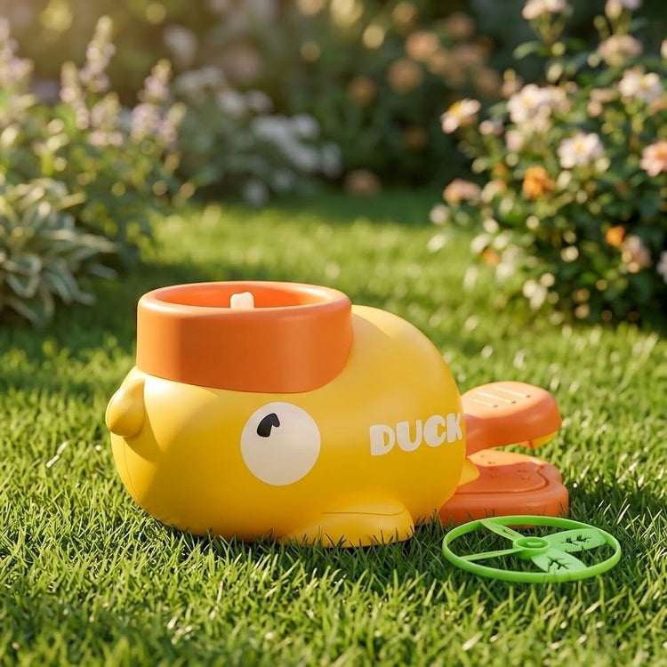 A yellow duck-shaped plastic disc launcher with orange pedals sits beside a green disc on grass in a sunny garden.
