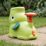 Rear three-quarter view of the green elephant disc launcher shows its coral pedal, small tail and teal ear on a garden path.