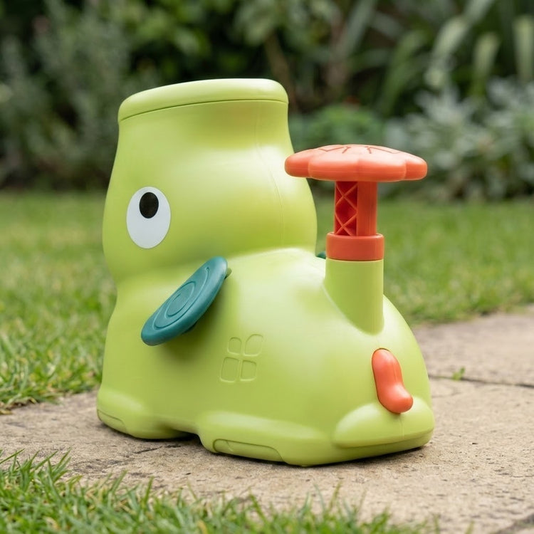 Rear three-quarter view of the green elephant disc launcher shows its coral pedal, small tail and teal ear on a garden path.