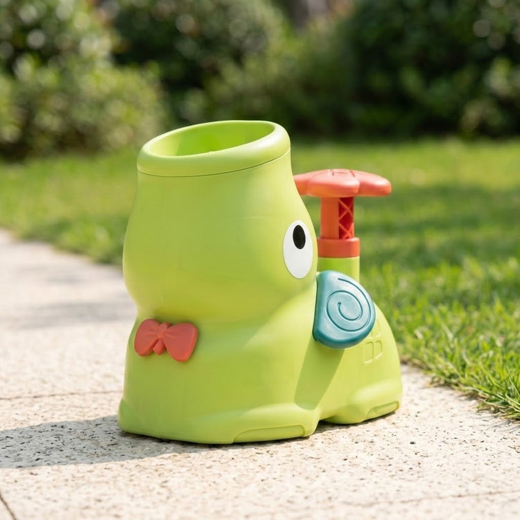 Green elephant-shaped disc launcher stands alone on a pale outdoor path, with its open top, coral bow and teal ear visible.