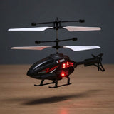 A black remote control toy helicopter with white blades and red LED lights, hovering over a wooden surface against a dark gray background.