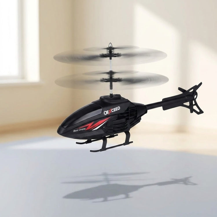 A black remote control helicopter with red and white accents hovers indoors with blurred spinning rotors and a shadow below.