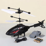 Black remote control toy helicopter with white rotors, shown with a gray toy truck, USB charging cable, and four batteries on a light beige background.