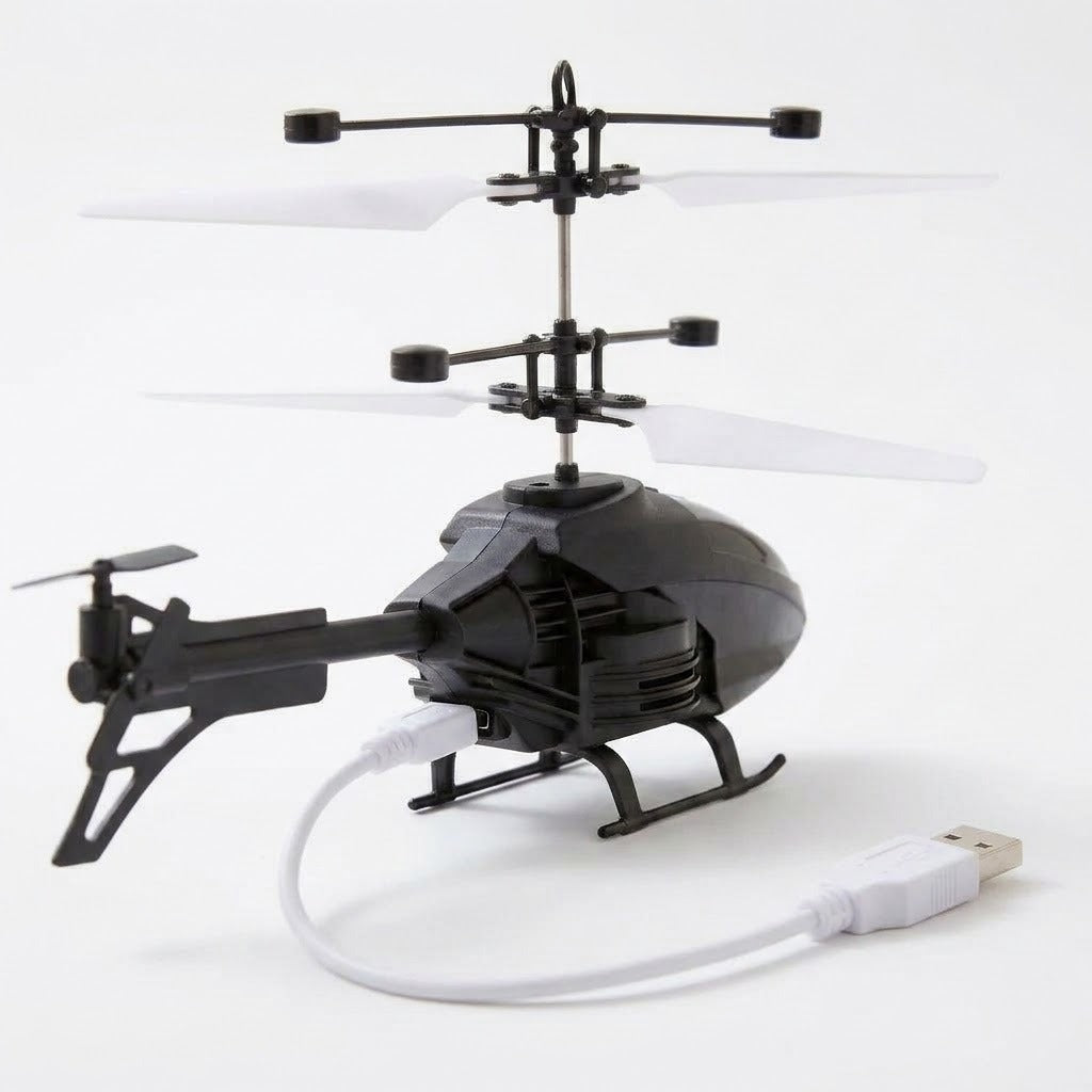 A black remote control helicopter with white rotor blades sits on a white surface with a white USB charging cable connected.