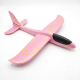 A pink foam toy glider with yellow speckles, curved wingtips, and a black cockpit rests on a white background.