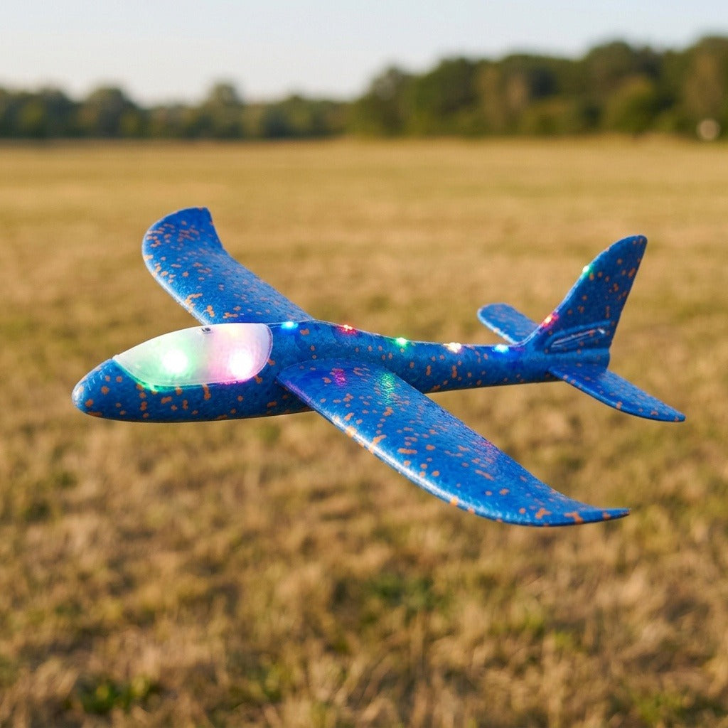 A blue foam toy glider with orange speckles and glowing multicolored lights appears above a dry grass field.