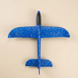A blue speckled foam toy glider with a black cockpit rests on a beige background, viewed directly from above.