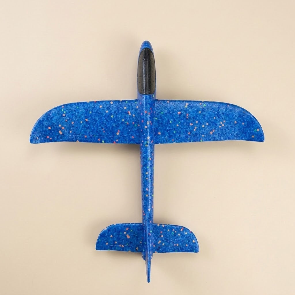 A blue speckled foam toy glider with a black cockpit rests on a beige background, viewed directly from above.