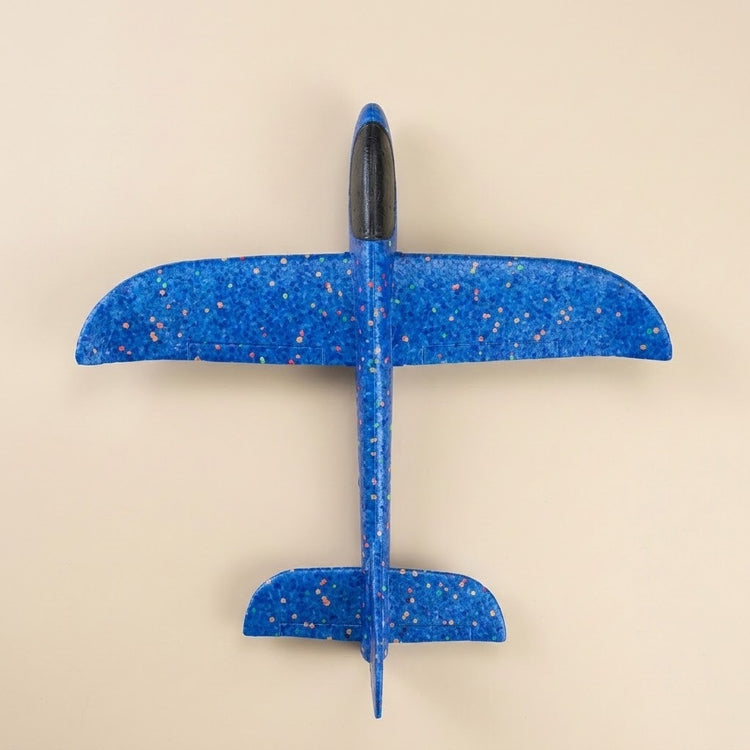 A blue speckled foam toy glider with a black cockpit rests on a beige background, viewed directly from above.