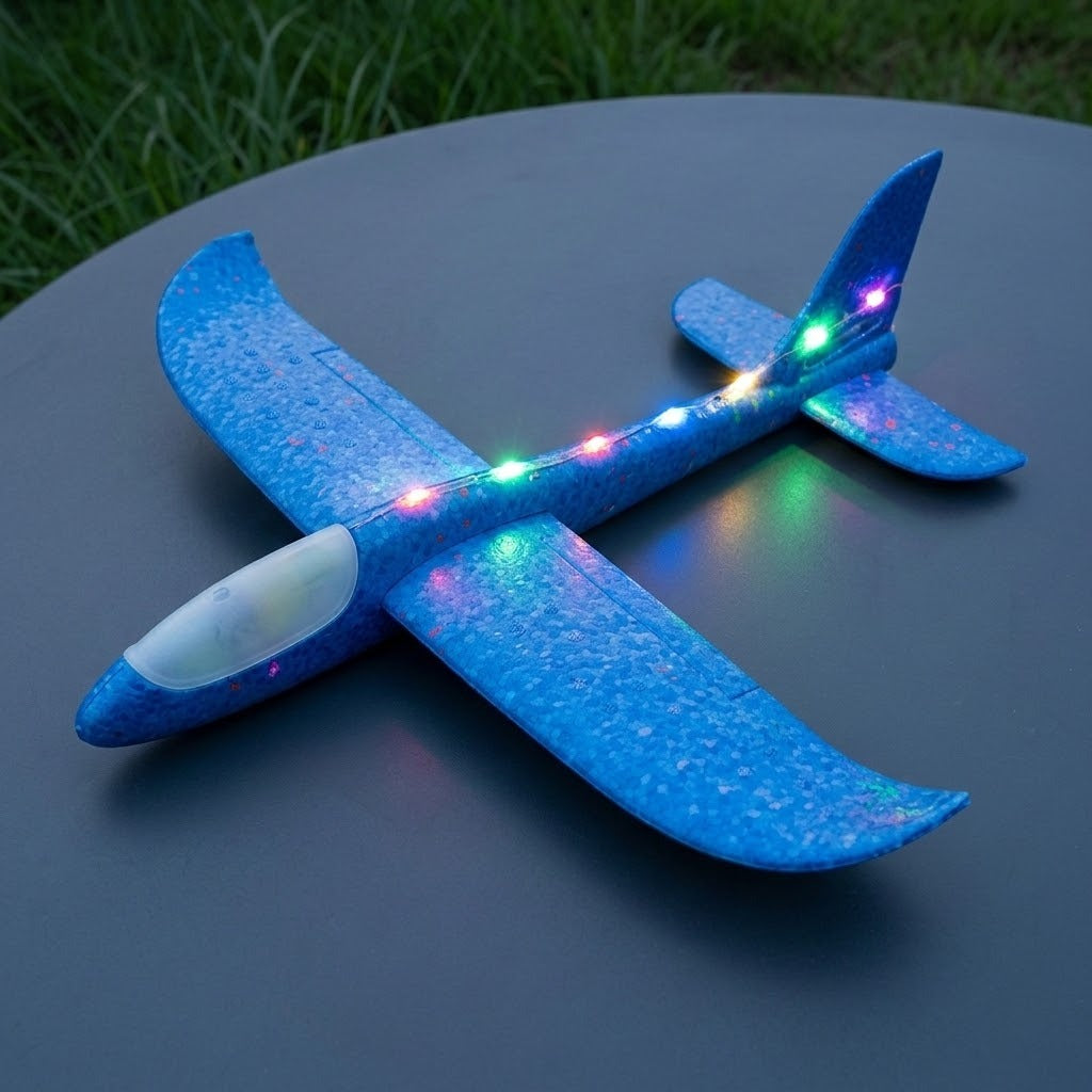 A blue foam toy glider with multicoloured LED lights rests on a round grey table beside grass.