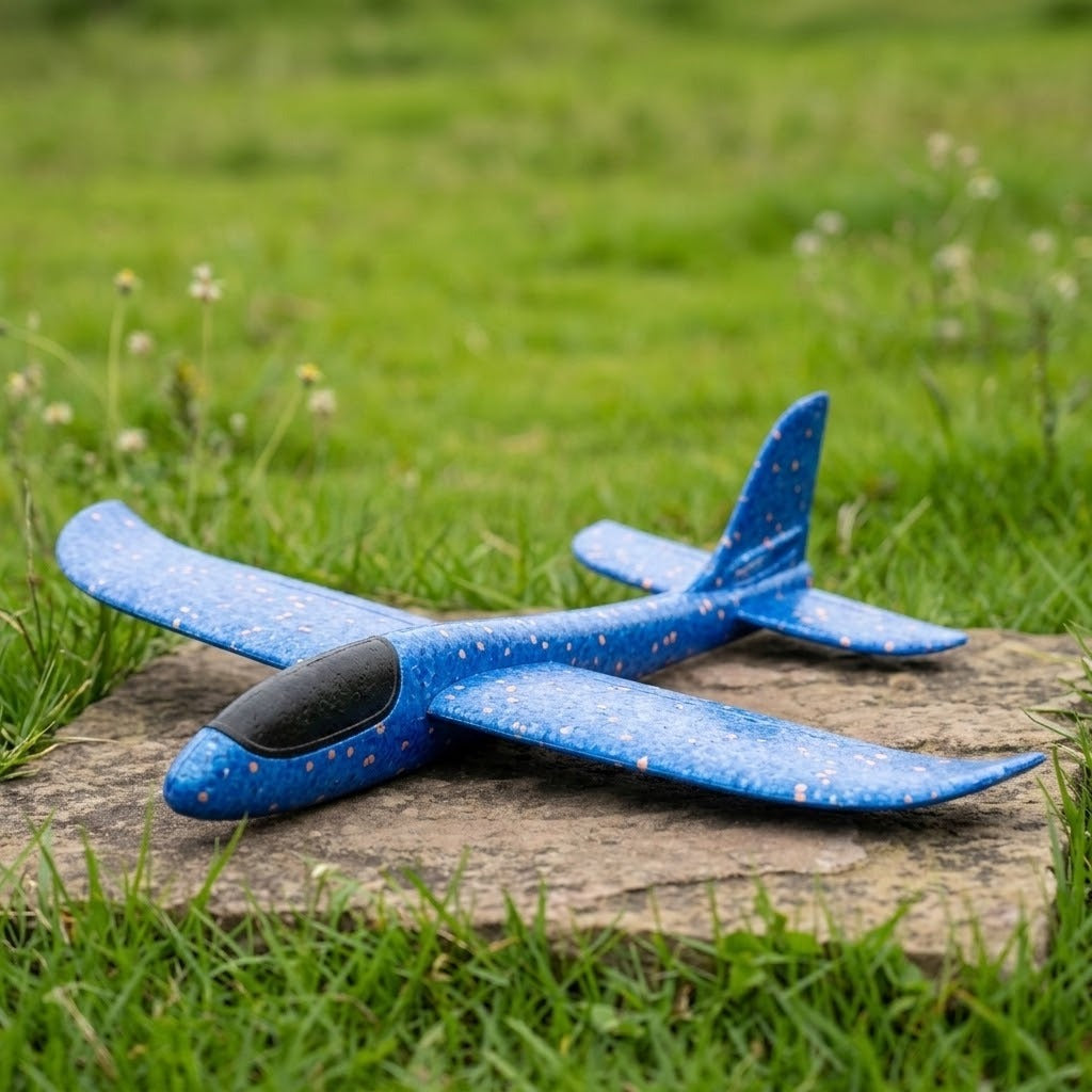 A blue speckled foam toy glider with a black cockpit rests on a stone slab surrounded by grass.