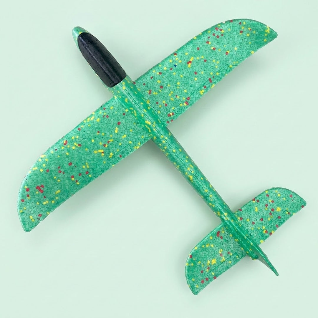 A green foam toy glider with multicoloured speckles and a black cockpit lies diagonally across a pale mint background.