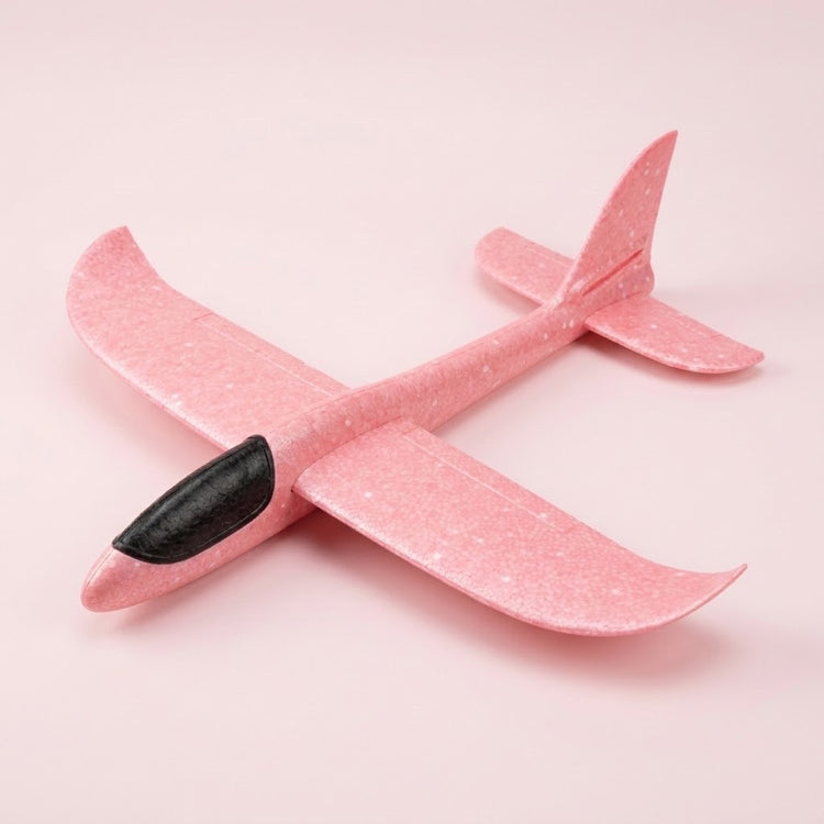 A pink foam toy glider with a black cockpit and upturned wingtips rests on a pale pink background.