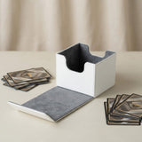 An open white deck box with gray lining and an extended flap sits beside stacks of cards on a beige tabletop.