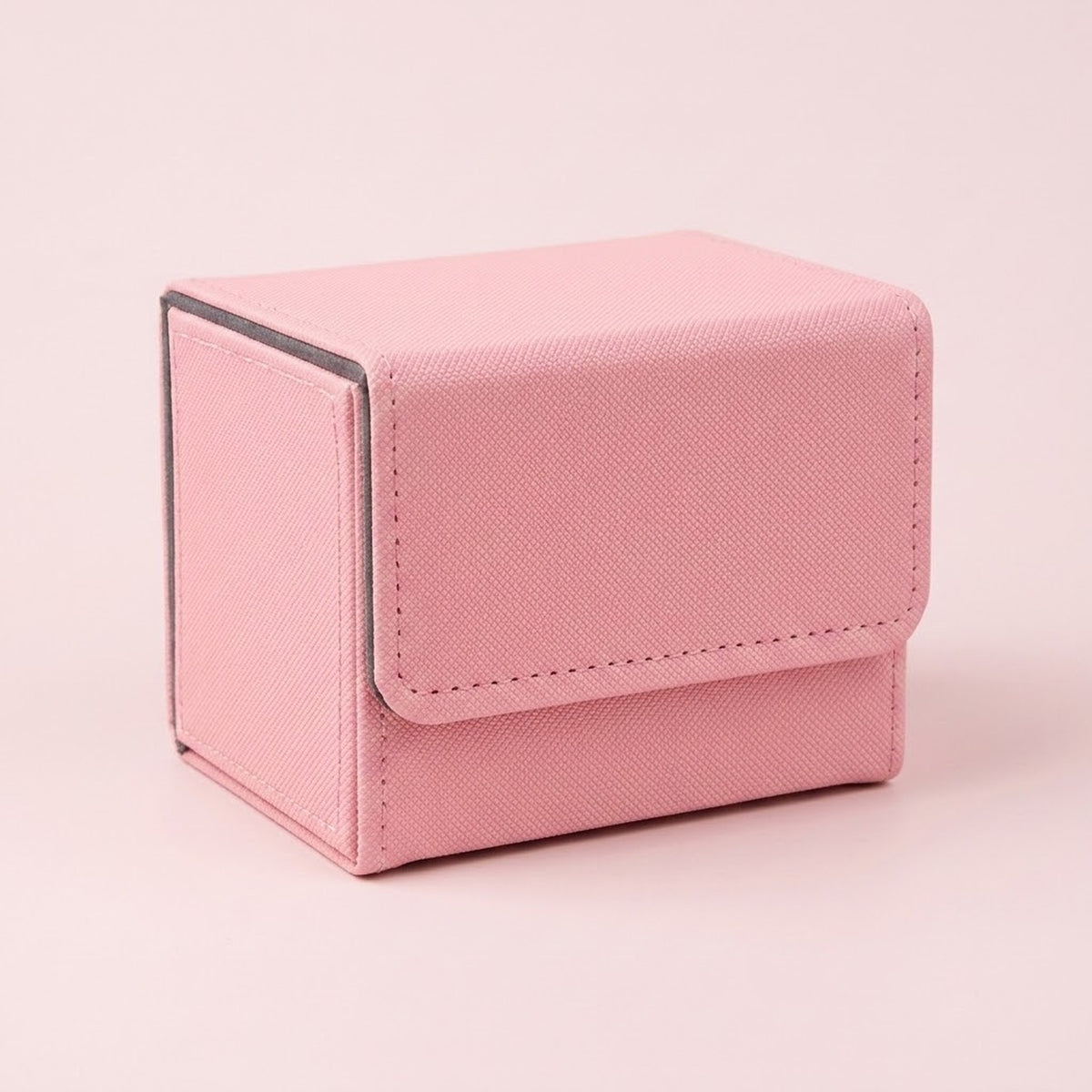 A pink textured deck box with gray edging and a closed stitched flap sits on a pale pink background.