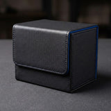 A closed black deck box with blue trim and a textured stitched flap rests on a dark gray surface against a blurred background.